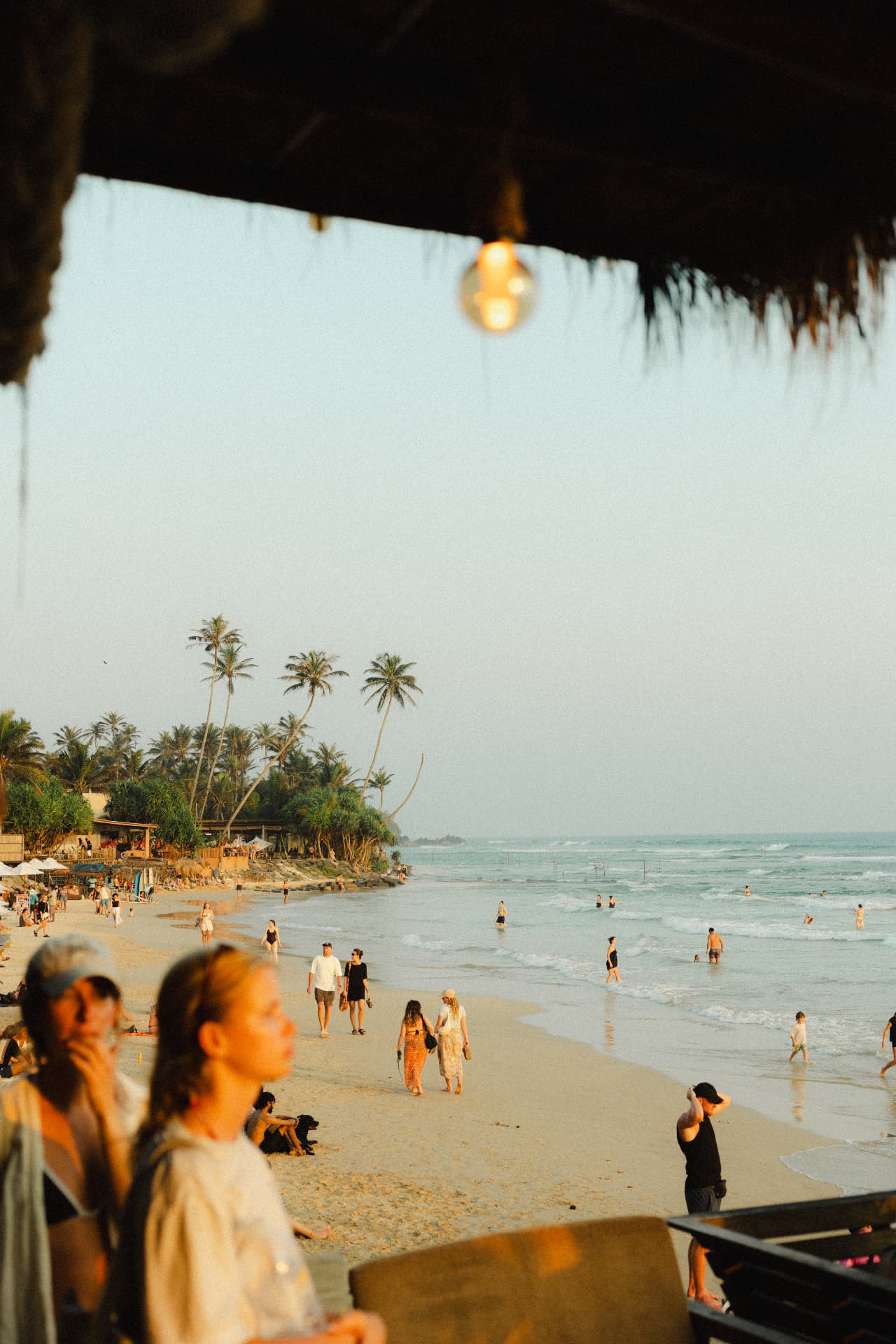 Golden evening light over Weligama Bay, seen from the Ceylon Sliders café as surfers and wanderers share the beach